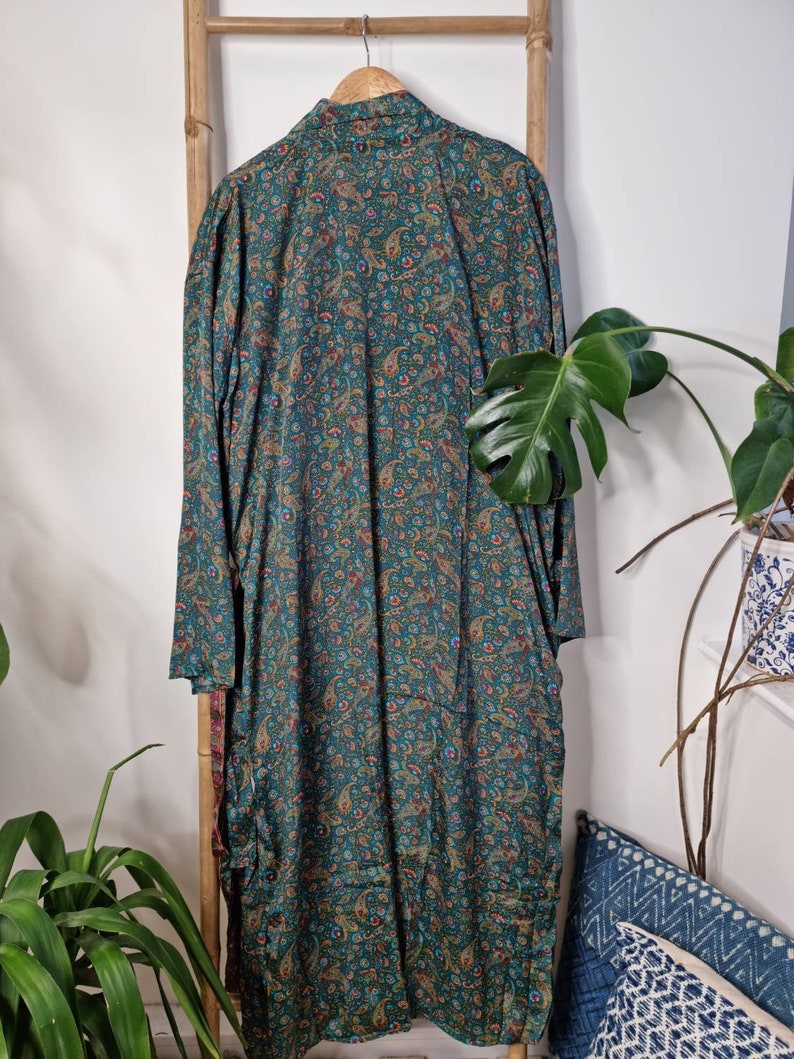 May include: A long-sleeved robe featuring a dark teal base color with an intricate, multi-colored paisley pattern in shades of gold, red, and blue. The garment has a classic collar, a button-down front, and a loose, flowing silhouette.