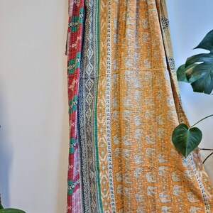 May include: A kantha quilt with a patchwork design featuring a red, green and black border. The centre of the quilt is a mustard yellow fabric with a white elephant print.