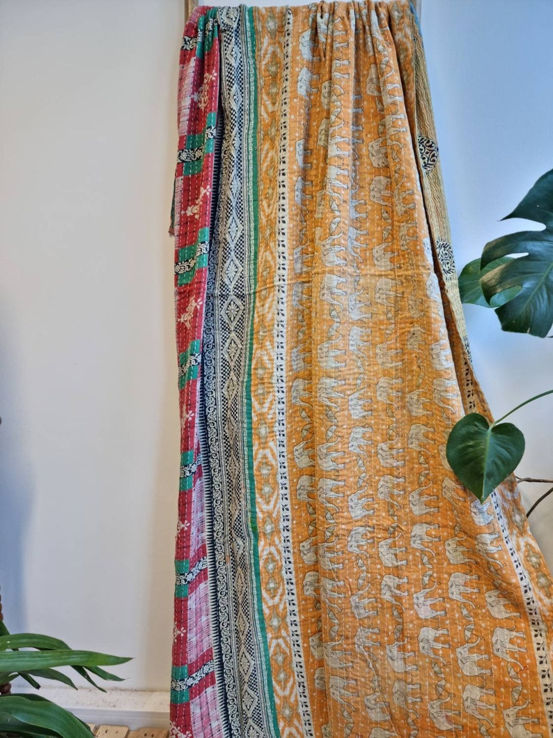 May include: A kantha quilt with a patchwork design featuring a red, green and black border. The centre of the quilt is a mustard yellow fabric with a white elephant print.