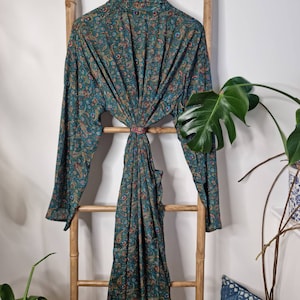 May include: A long-sleeved robe featuring a dark teal base color with an intricate, multi-colored paisley pattern in shades of orange, red, and blue. The garment has a wrap-style front with a matching fabric tie at the waist and a collar.
