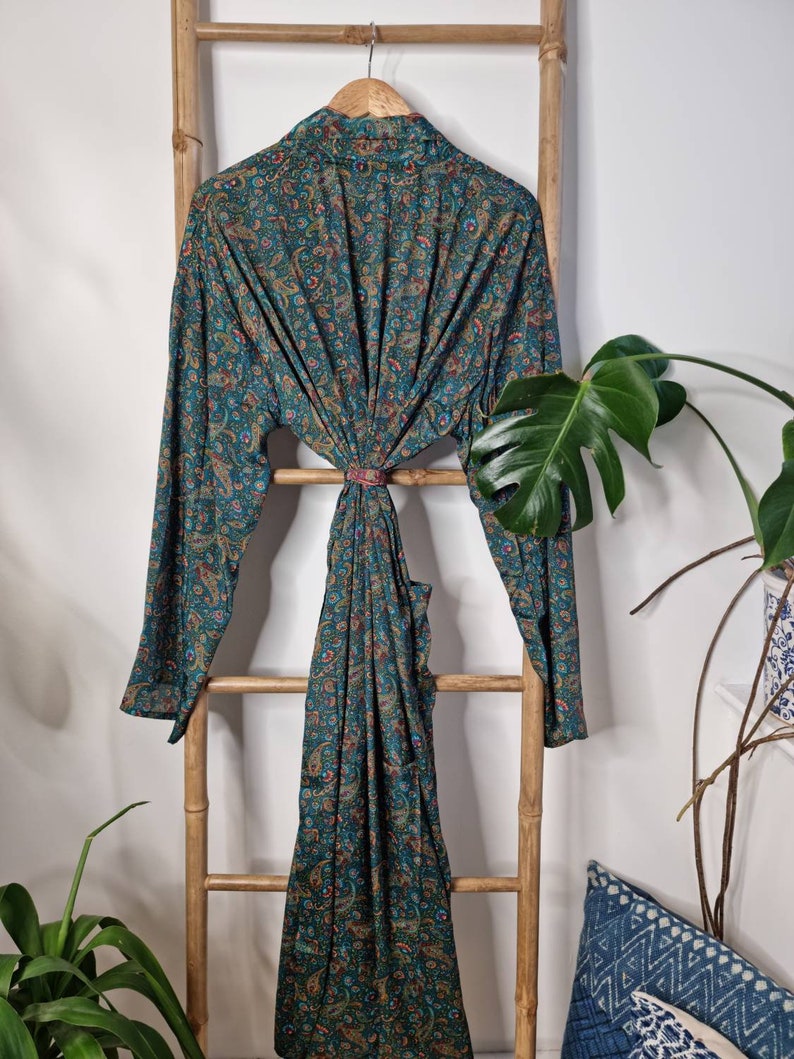 May include: A long-sleeved robe featuring a dark teal base color with an intricate, multi-colored paisley pattern in shades of orange, red, and blue. The garment has a wrap-style front with a matching fabric tie at the waist and a collar.