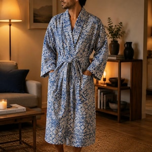 May include: A long-sleeved robe featuring a blue and white tile-inspired geometric pattern. The garment includes a shawl collar, a matching fabric tie belt at the waist, and two large patch pockets on the front. The robe falls to the mid-calf.