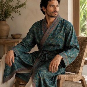 May include: A teal robe featuring a detailed multicolored floral and paisley pattern throughout. The garment includes long sleeves, a wrap-front design with a matching fabric tie belt, and contrasting decorative trim along the collar and cuffs.
