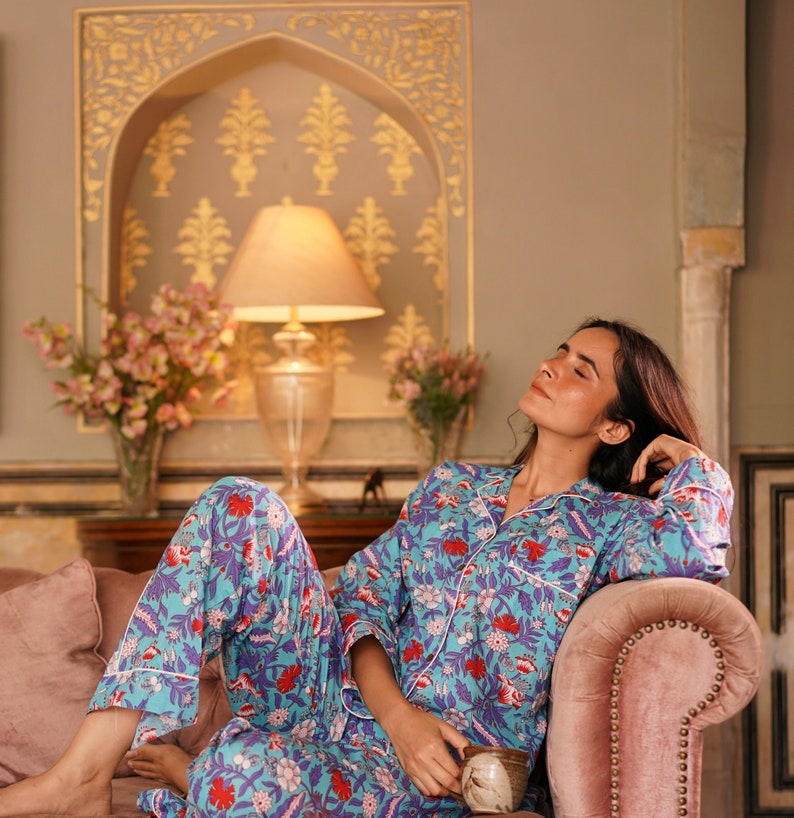 Peut inclure: Une femme portant un pyjama bleu et blanc &agrave; fleurs avec des accents rouges, se relaxant sur un canap&eacute; rose. Elle tient une tasse dans sa main.