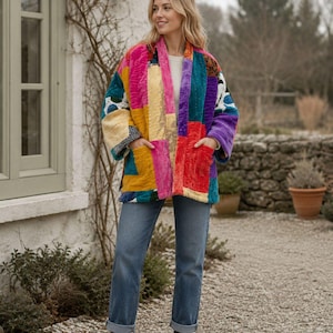 May include: A quilted jacket featuring a vibrant patchwork design with various colours including hot pink, mustard yellow, teal, and red. The jacket has an open front, long sleeves, and two front pockets, worn over a white top and blue jeans.