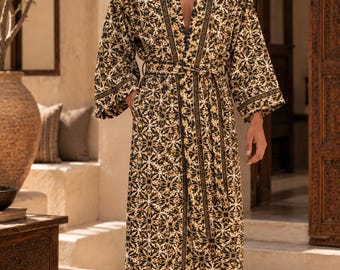 May include: A long-sleeved robe featuring a repeating geometric floral pattern in shades of dark blue, mustard yellow, and white. The garment includes a matching fabric belt at the waist, wide sleeves, and a contrasting dark trim along the front opening.