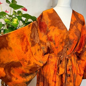 May include: A vibrant orange and brown tie-dye patterned kimono robe with a V-neck and a matching belt. The robe is displayed on a white mannequin. The sleeves are wide.