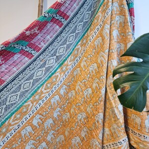 May include: A kantha quilt with a patchwork design featuring a red, green and blue border. The centre of the quilt is a yellow fabric with a white elephant pattern.