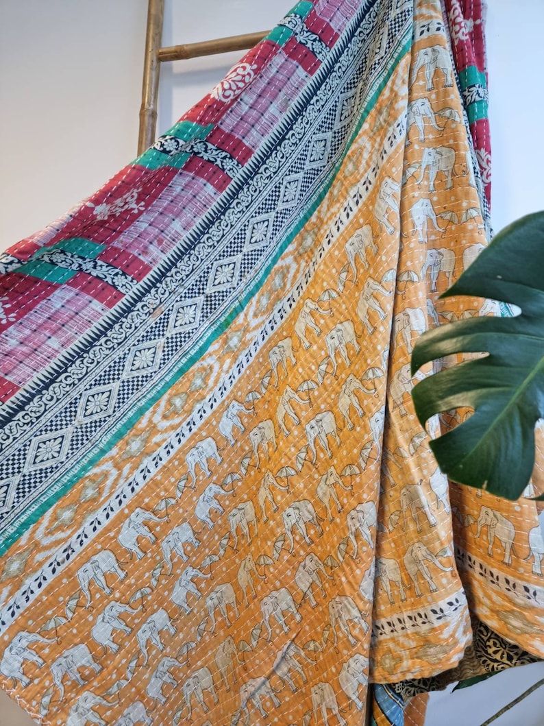 May include: A kantha quilt with a patchwork design featuring a red, green and blue border. The centre of the quilt is a yellow fabric with a white elephant pattern.