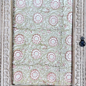 May include: A rectangular wooden frame with a carved floral design surrounds a floral patterned fabric. The fabric features a repeating pattern of pink and white flowers on a light green background. The frame has a distressed, off-white finish.