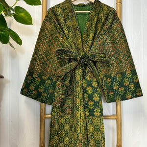 May include: A green and yellow patterned kimono robe with a matching tie belt. The robe is hanging on a wooden hanger and displayed on a bamboo ladder. The fabric features a repeating floral design.