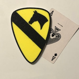 May include: A yellow and black patch with a horse head silhouette. The patch is shaped like a guitar pick and has a black stripe across it. The patch is next to an ace of spades playing card.