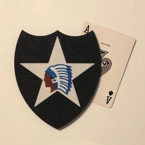 May include: A black and white shield-shaped patch with a white star and a blue and red Native American head inside the star. The patch is on a white background.