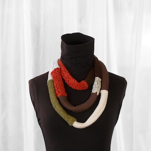 Puede incluir: Una bufanda de punto multicolor con secciones marrones, blancas, verdes y rojas. La bufanda está enroscada alrededor de un cuello de tortuga negro.