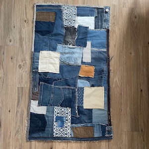 Op de afbeelding: Een patchworkdeken gemaakt van denimstof in verschillende tinten blauw, met wat bruine en beige vlekken. De deken is gemaakt van veel verschillende denimstukken, die aan elkaar zijn genaaid om een uniek en interessant ontwerp te creëren.