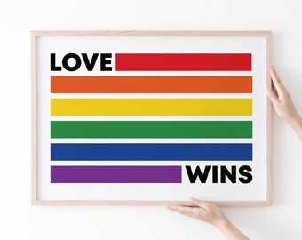 May include: A framed print featuring the colors of the rainbow flag. The word "LOVE" is above the rainbow stripes, and the word "WINS" is below. The print is in a light-colored wooden frame.