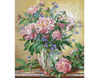 Puede incluir: Un ramo de peonías rosas y flores azules en un jarrón de vidrio transparente sobre una mesa de madera.