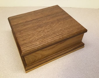 May include: A wooden box with a light brown finish. The box has a hinged lid and a decorative trim around the edges.
