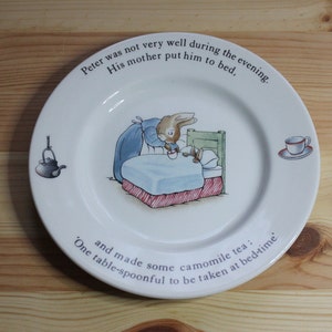 May include: A white ceramic plate with a blue and white illustration of a bunny in bed. The plate has text that reads "Peter was not very well during the evening. His mother put him to bed, and made some camomile tea: One table-spoonful to be taken at bed-time."