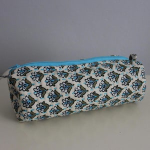 May include: A cylindrical pencil case with a blue zipper and a white background with a blue and green floral pattern.