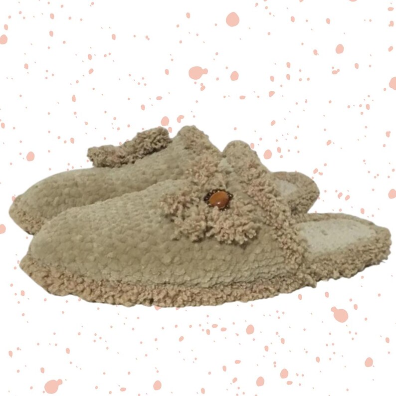 May include: A pair of beige fuzzy slippers with a decorative button on the top. The slippers have a fluffy trim around the edges.