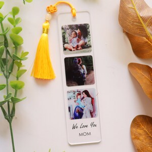 May include: A clear acrylic bookmark with three photo inserts and a yellow tassel. The photos show a mother and child. The bookmark has the text "We Love You MOM" printed on the bottom.