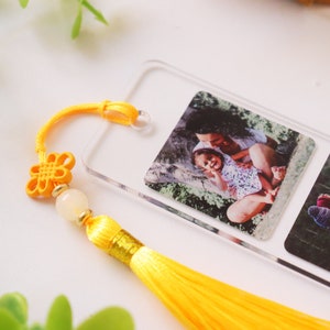 May include: A clear acrylic bookmark with two photo slots. The bookmark features a yellow tassel and a yellow knot charm. The photos show a mother and daughter in a park.
