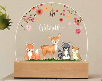 May include: A wooden night light with a clear acrylic dome featuring a deer, fox, raccoon, and owl surrounded by pink, orange, and green flowers. The name "Wilmoth" is written on the dome.