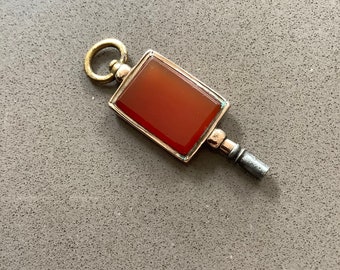 May include: A gold-toned pocket watch key with a red carnelian stone set in a square frame.