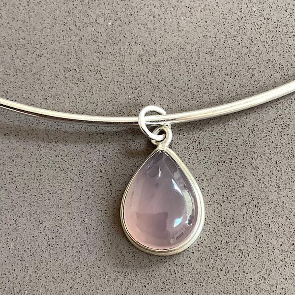 May include: A silver-toned metal collar necklace featuring a single teardrop-shaped pendant with a smooth, translucent pale pink stone set in a silver-colored bezel. The pendant hangs from a simple, polished silver-toned metal wire neck ring.