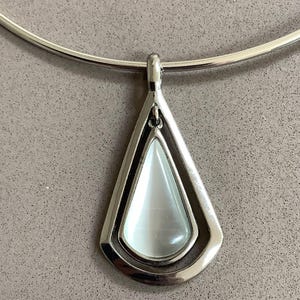 May include: A silver pendant necklace. The pendant has a teardrop shape with a pearly white stone centre. It's framed by a double-layered silver metal design and hangs from a thin, curved silver necklace.