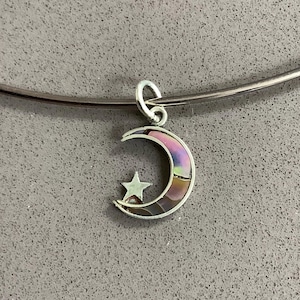 May include: A silver necklace with a crescent moon pendant and star detail. The moon pendant has a mother-of-pearl inlay with iridescent pink and purple tones. The necklace is set against a grey background.