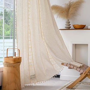 Può includere: Tenda in lino beige con dettagli ricamati geometrici e bordi con nappe. La tenda è vicino a una finestra, con uno sgabello e un cestino di legno in primo piano. Un vaso e una ciotola decorativi sono su una mensola.