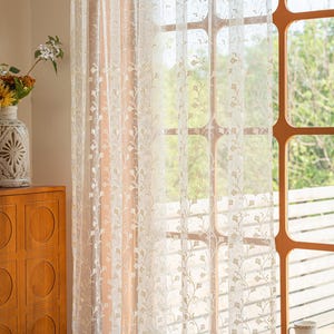 May include: A sheer white curtain panel featuring a delicate, repeating vertical pattern of embroidered light brown vines and small leaves. The lightweight fabric allows soft natural light to filter through, highlighting the intricate botanical design.