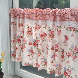 May include: Floral patterned window curtains. The curtains feature a cream background with red, pink, and purple roses. The top of the curtains has a red and white checkered pattern with a white lace trim. The curtains are hanging in front of a window.
