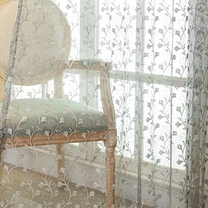 May include: A sheer, light-colored curtain panel featuring an intricate, vertical embroidered pattern of delicate, winding vines with small, stylized leaves and buds. The fabric is semi-transparent, allowing light to pass through the embroidery.