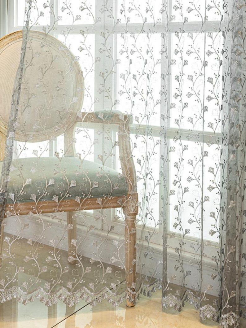 May include: A sheer, light-colored curtain panel featuring an intricate, vertical embroidered pattern of delicate, winding vines with small, stylized leaves and buds. The fabric is semi-transparent, allowing light to pass through the embroidery.