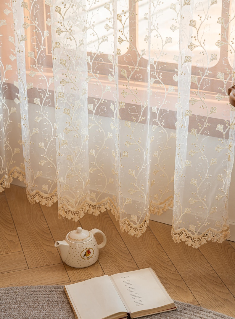 May include: Sheer white curtains featuring delicate embroidered vine patterns with small leaves and a scalloped lace trim along the bottom edge. The fabric is translucent, allowing light to pass through while displaying the intricate floral embroidery.