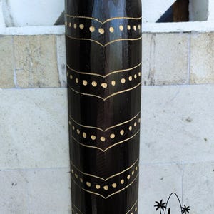 May include: A black wooden cylinder with a decorative pattern of gold dots and lines. The cylinder is carved with a repeating design of curved lines and dots.
