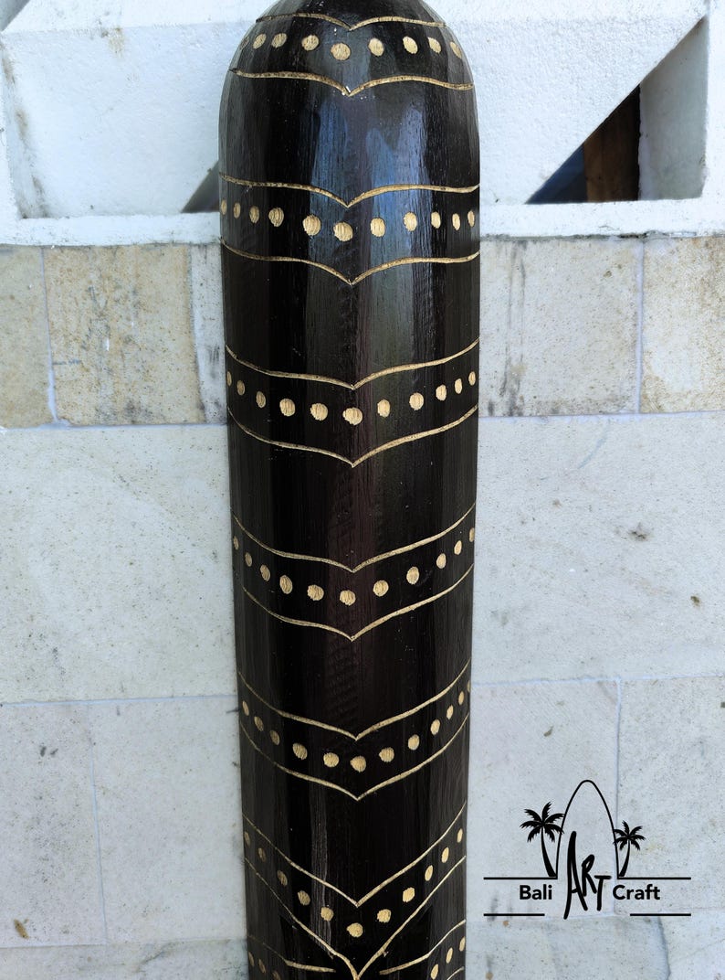 May include: A black wooden cylinder with a decorative pattern of gold dots and lines. The cylinder is carved with a repeating design of curved lines and dots.
