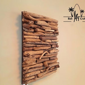 May include: A square wall art piece made of driftwood arranged in a layered pattern. The driftwood is a light brown color and is set against a black background. The piece is titled "Bali Art Craft".