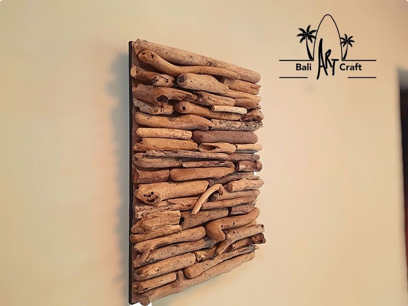 May include: A square wall art piece made of driftwood arranged in a layered pattern. The driftwood is a light brown color and is set against a black background. The piece is titled "Bali Art Craft".
