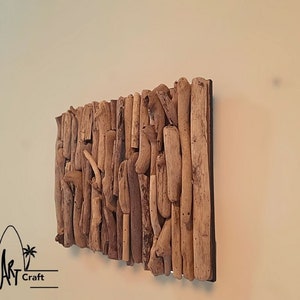 May include: A wall art piece made of driftwood arranged in a rectangular shape. The driftwood is a variety of shades of brown and beige. The piece is mounted on a black background.