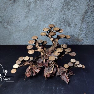 Puede incluir: Escultura de bons&aacute;i artesanal hecha de madera natural y monedas de metal. El &aacute;rbol presenta un tronco y ramas detallados con hojas en forma de moneda. La escultura se encuentra sobre un fondo oscuro, mostrando los intrincados detalles de la obra.