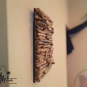 May include: A wall decor piece made of driftwood arranged in a rectangular shape. The driftwood is a light brown color and is mounted on a black background.
