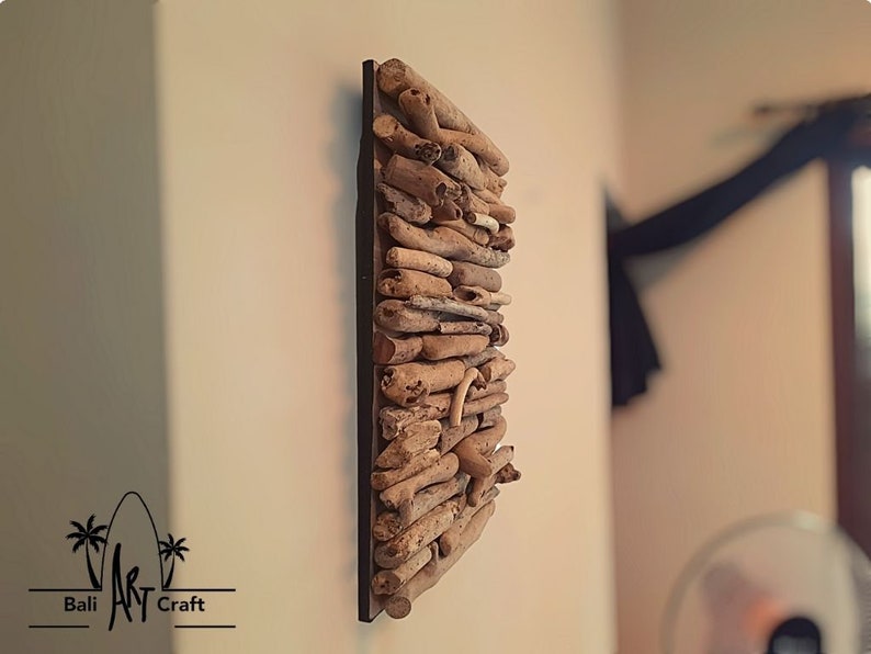 May include: A wall decor piece made of driftwood arranged in a rectangular shape. The driftwood is a light brown color and is mounted on a black background.