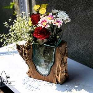May include: A wooden vase with a glass insert, holding a bouquet of red, white and yellow flowers. The vase is made from a piece of driftwood with a natural, rustic look.