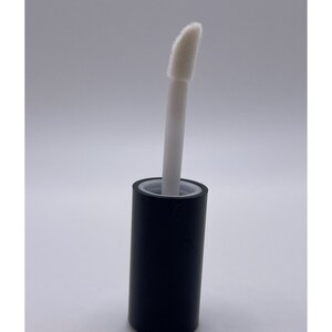 Puede incluir: Un tubo negro con una punta aplicadora blanca. La punta aplicadora es un peque&ntilde;o pincel en &aacute;ngulo.