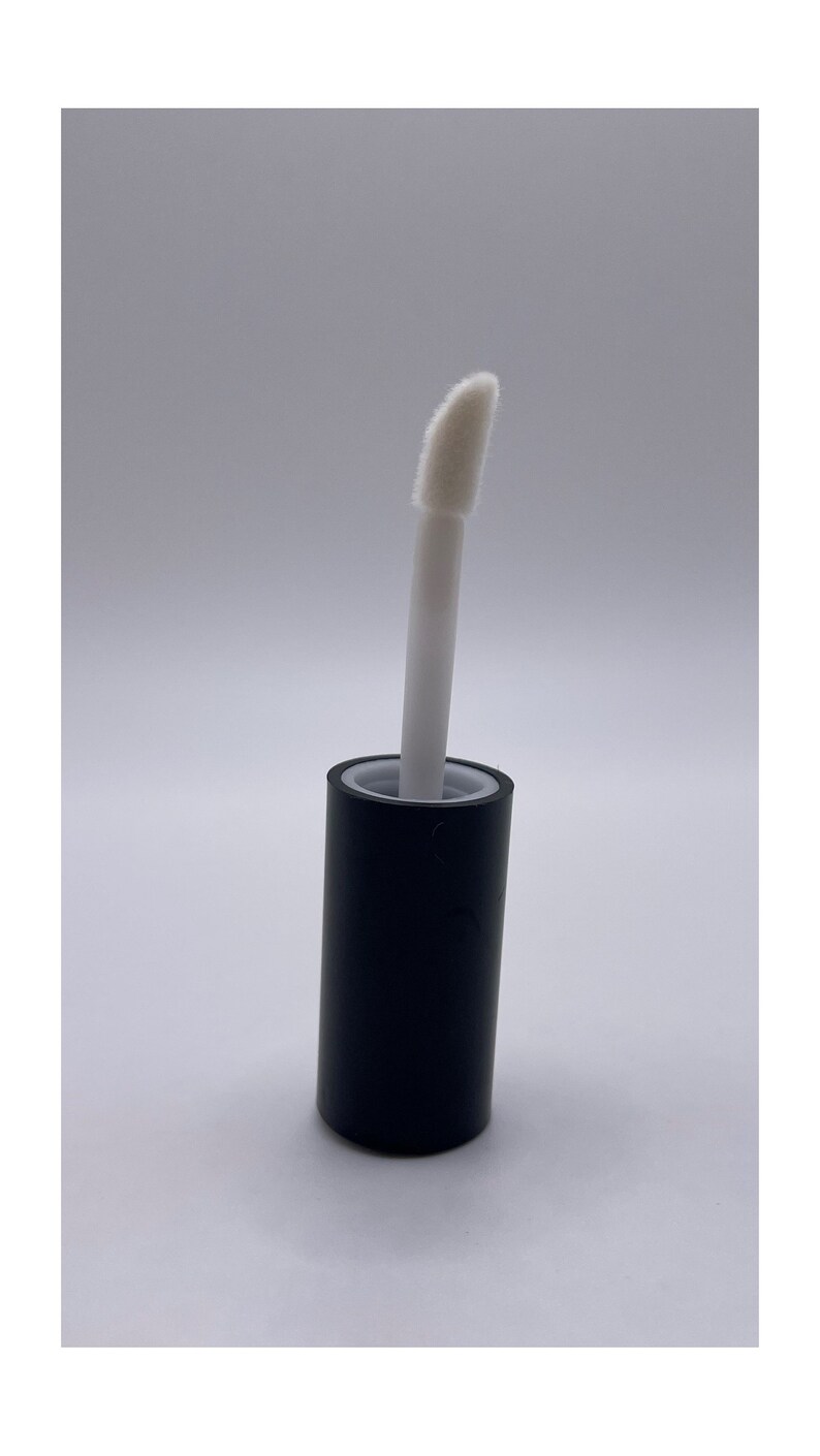 Puede incluir: Un tubo negro con una punta aplicadora blanca. La punta aplicadora es un peque&ntilde;o pincel en &aacute;ngulo.