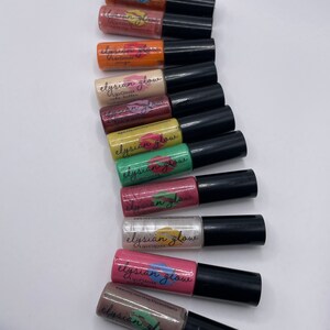 Puede incluir: Un conjunto de diez frascos peque&ntilde;os de brillo de labios en varios colores, incluyendo naranja, amarillo, verde, rosa y marr&oacute;n. Cada frasco tiene una tapa negra y una etiqueta que dice "elysian glow" y "lip gloss".